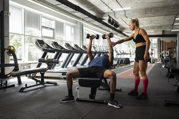 Mejores gimnasios en CDMX - Instructora de gimnasio orienta a un hombre cómo hacer ejercicio con pesas