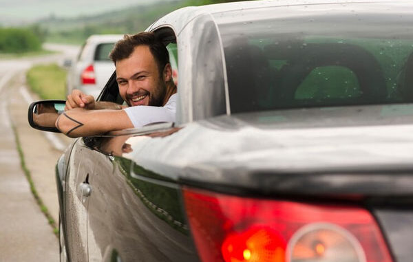 Joven sonríe mientras conduce su nuevo coche deportivo