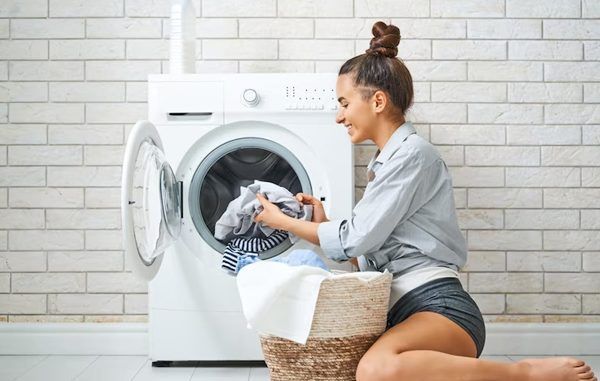 Marcas de lavadoras de ropa - Joven saca la ropa limpia y lavada de una lavadora de carga frontal