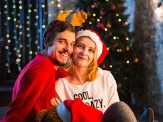 Navidad en CDMX - Hombre y mujer abrazados y sentados en el piso con gorros navideños delante de un árbol de Navidad