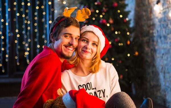 Navidad en CDMX - Hombre y mujer abrazados y sentados en el piso con gorros navideños delante de un árbol de Navidad
