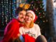 Navidad en CDMX - Hombre y mujer abrazados y sentados en el piso con gorros navideños delante de un árbol de Navidad