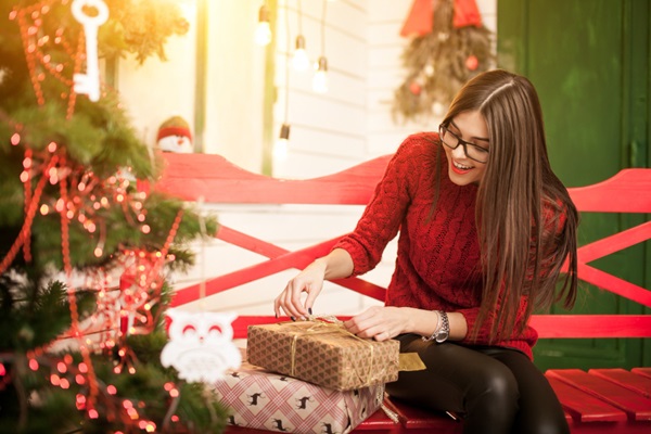 Navidad en CDMX - Mujer joven sentada en una banca roja junto a un árbol abriendo regalos de navidad