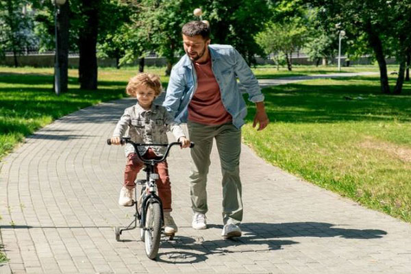 Actividades para año nuevo - Hombre se toma una tarde en el parque para enseñar a su hijo a manejar bicicleta