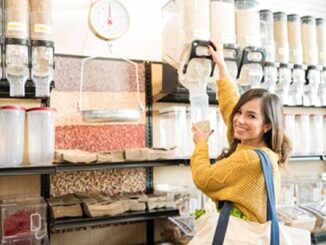 Tiendas a granel - Mujer feliz usando un dispensador de productos a granel para llenar un envase con frutos secos