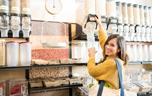Tiendas a granel - Mujer feliz usando un dispensador de productos a granel para llenar un envase con frutos secos