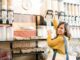 Tiendas a granel - Mujer feliz usando un dispensador de productos a granel para llenar un envase con frutos secos