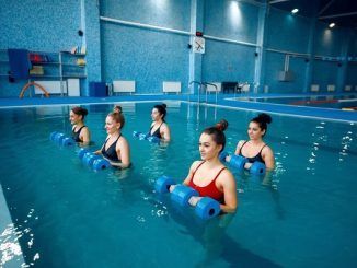 Escuelas de clases de natación - Mujeres jóvenes toman clases de aqua aerobics para aumentar la flexibilidad y tonificar los músculos