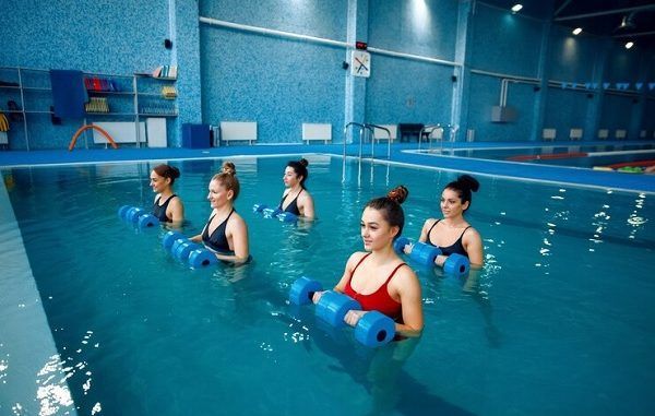 Escuelas de clases de natación - Mujeres jóvenes toman clases de aqua aerobics para aumentar la flexibilidad y tonificar los músculos
