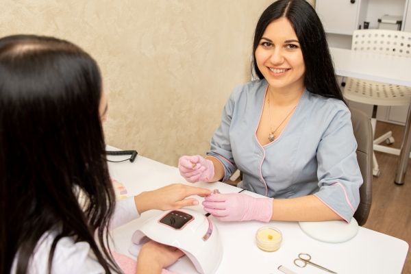 Mejores salones de uñas de CDMX - Manicurista aplica un esmalte y trabaja en la decoración y en el secado de la manos de una cliente