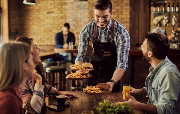 Mejores restaurantes cool CDMX - Mesero sirve una orden de papas y hamburguesas atendiendo el pedido de un grupo de comensales