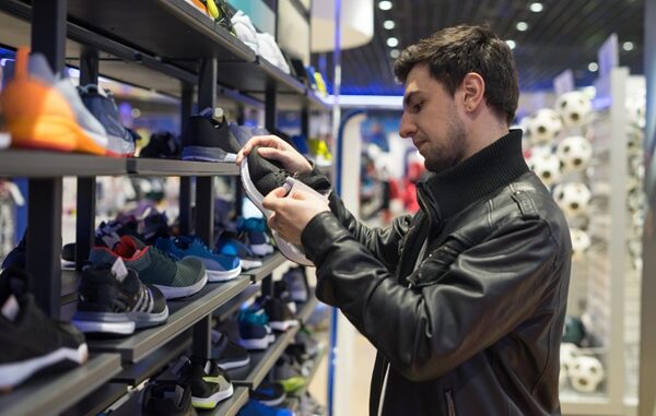 Tiendas de calzado deportivo - Hombre joven observando diversos modelos de zapatos deportivos para escoger el mejor tenis