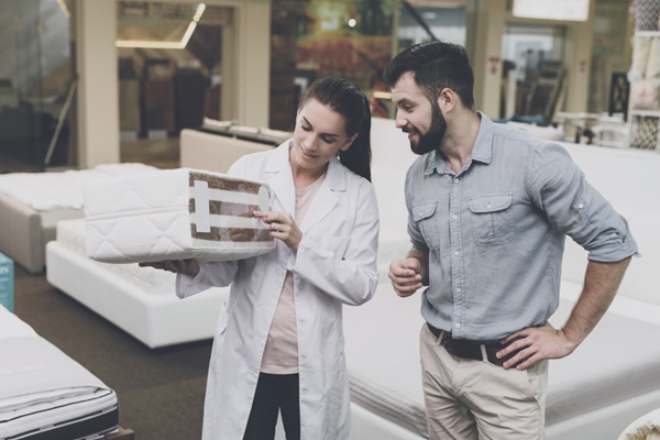 Tiendas de colchones - Asesora de ventas de una tienda de colchones mostrándole a un hombre las diferentes tecnologías para lograr un descanso de calidad