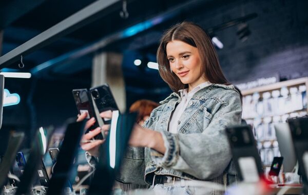 Tiendas de tecnología - Mujer joven comparando teléfonos nuevos en una tienda de tecnología en CDMX para elegir el mejor