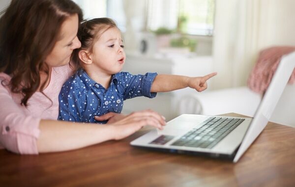 Tiendas para bebé online - Mujer con una niña en sus brazos frente a la computadora haciendo compras en línea de productos para bebés