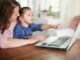 Tiendas para bebé online - Mujer con una niña en sus brazos frente a la computadora haciendo compras en línea de productos para bebés