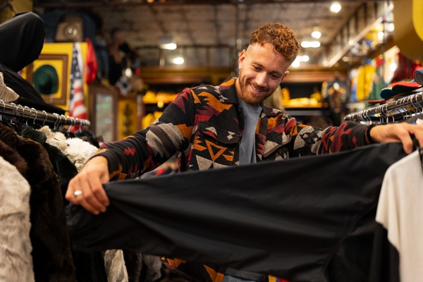 Tiendas de segunda mano en CDMX - Hombre en una tienda de ropa usada observando una chamarra de marca a precios económicos