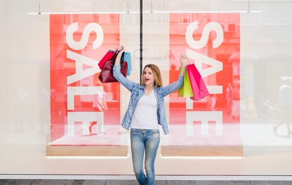 Tiendas outlet - Mujer feliz sosteniendo varias bolsas de compras frente a una tienda outlet en CDMX
