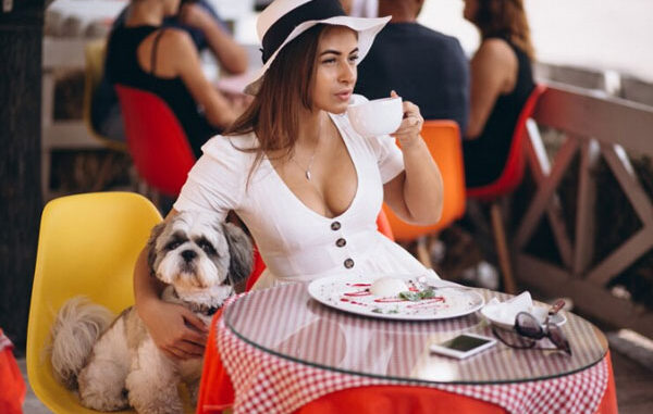 Joven toma un postre y una taza de café en compañía de su perro