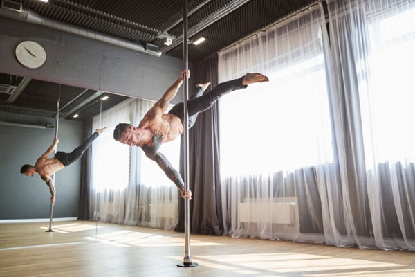 Hombre músculo entrena y trabaja en la expresión corporal con ayuda de una barra de pol dance 