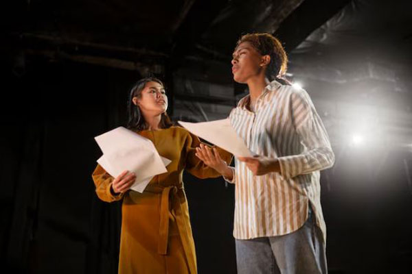 Jóvenes ensayan una obra de teatro interpretando diversos personajes sobre el escenario 