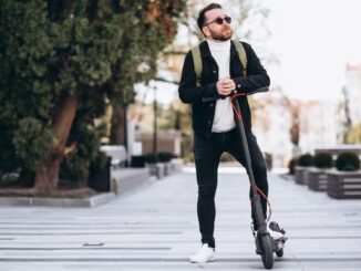 Patines eléctricos - hombre vestido con camisa blanca chaqueta negra y jeans negros, usando lentes de sol, posando junto con su patín eléctrico en CDMX