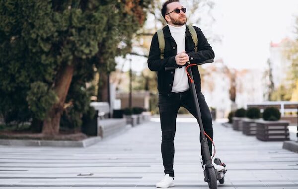 Patines eléctricos - hombre vestido con camisa blanca chaqueta negra y jeans negros, usando lentes de sol, posando junto con su patín eléctrico en CDMX