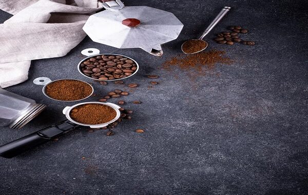 Las mejores marcas de café de CDMX - Utensilios y materiales de café sobre una superficie oscura: cafetera moka, recipientes con granos y café molido, cuchara y algunos granos dispersos.