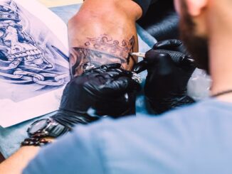 Los mejores estudios de tatuaje en CDMX - Tatuador trabajando en el brazo de un cliente. Se observa un diseño de tatuaje, que parece ser una calavera rodeada de cadenas.