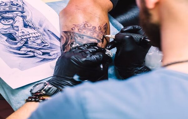 Los mejores estudios de tatuaje en CDMX - Tatuador trabajando en el brazo de un cliente. Se observa un diseño de tatuaje, que parece ser una calavera rodeada de cadenas.