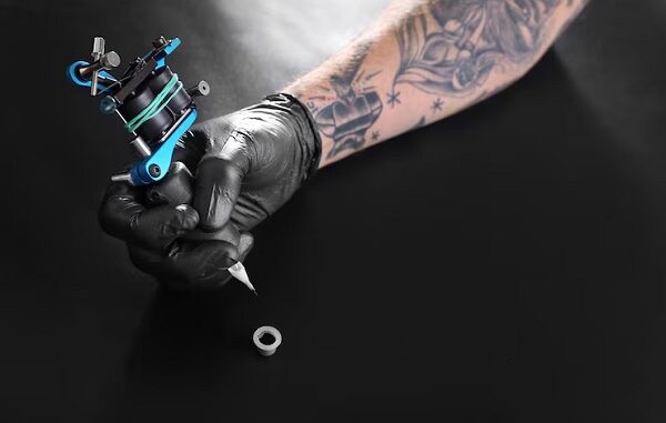 Los mejores tatuadores en CDMX - Mano de un tatuador sosteniendo una máquina de tatuar, la cual va a sumergir en tinta para empezar el tatuaje en CDMX