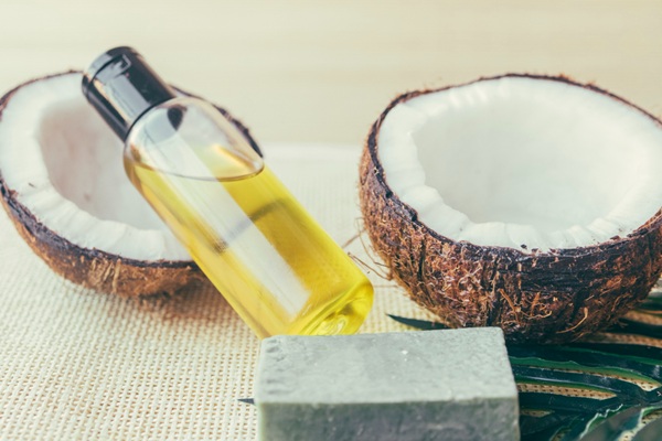 Remedios naturales para el cabello - Cocos abiertos junto a un recipiente con aceite de coco que ayuda nutrir las fibras capilares y detener la caída del cabello